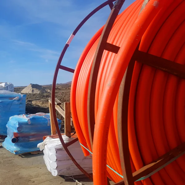 Roll of orange HDPE conduit on job site with pallets of elbows in the background